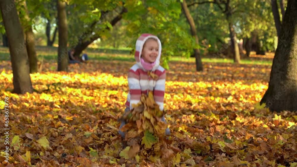 Happy girl laughs and throws leaves in autumn park at sunset. Child plays with maple leaves outdoors. Leisure, weekend in nature, active games Happy girl laughs and throws leaves in autumn park at sunset. Child plays with maple leaves outdoors. Leisure, weekend in nature, active games