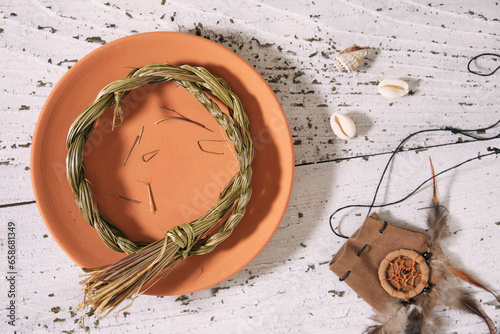 Sweetgrass braid (Hierochloe odorata), also called vanilla grass, on a clay plate and medicinal pouch on old white wood. High angle view, flat lay.