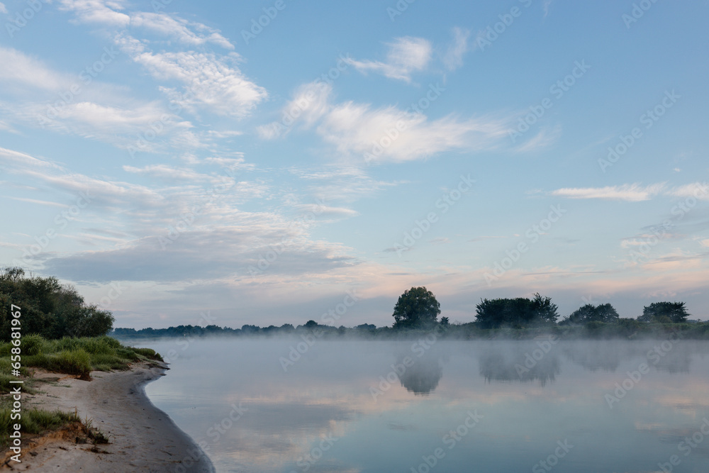 Beautiful landscape with a river and reflection, thick fog at dawn. Lake in the early morning in thick fog