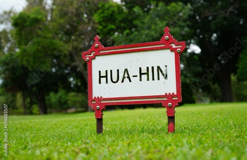 A red metal framed sign with black letters saying Hua Hin, which is a district of Thailand.