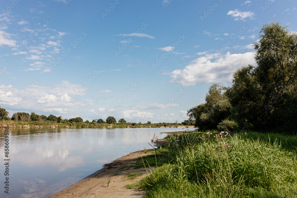 Beautiful summer landscape by the river with blue sky on a sunny summer day. Green grass and trees, on the shore of a lake in the sun. Camping. Summer background.