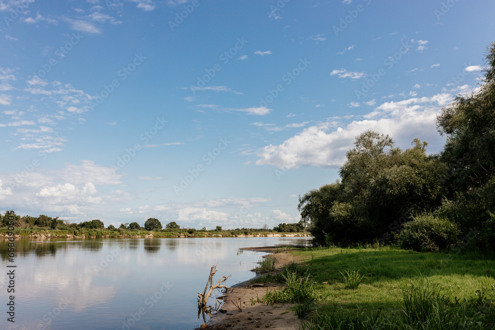 Beautiful summer landscape by the river with blue sky on a sunny summer day. Green grass and trees, on the shore of a lake in the sun. Camping. Summer background. Beautiful summer landscape by the river with blue sky on a sunny summer day. Green grass and trees, on the shore of a lake in the sun. Camping. Summer background.