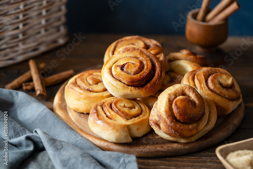 Homemade fresh baked cinnamon rolls on a wooden board with cinnamon sticks, sugar and napkin Wooden and dark background