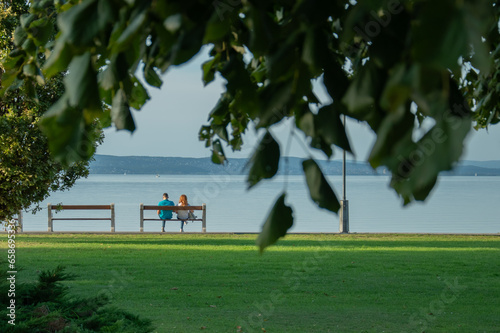 A young couple sitting on a bench at the lake