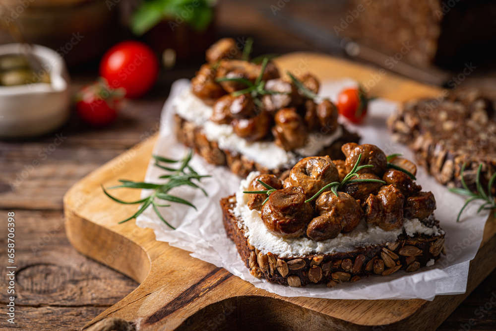 Whole grain rye bread toast with cream cheese or ricotta, mushroom and herbs on rustic wooden background.