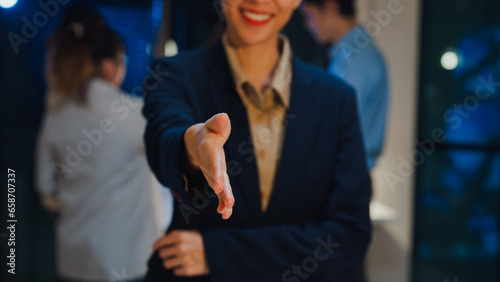 Portrait of successful executive businesswoman smart casual wear shaking hands and looking at camera and smiling happy in modern night office workplace. Partner cooperation, coworker teamwork concept.