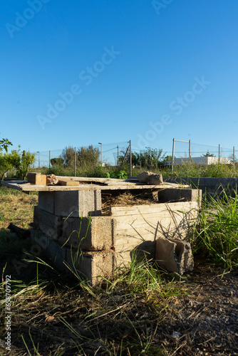 Vertical image of an organic composter built by hand with concrete blocks and old wood in a crop field.