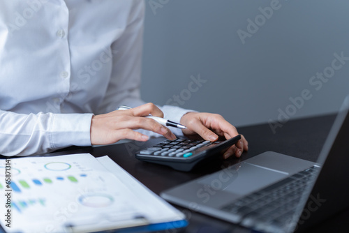 Business Documents concept: Employee Woman hands working with Smartphone, laptop, calculator, and chart on paper at the office.
