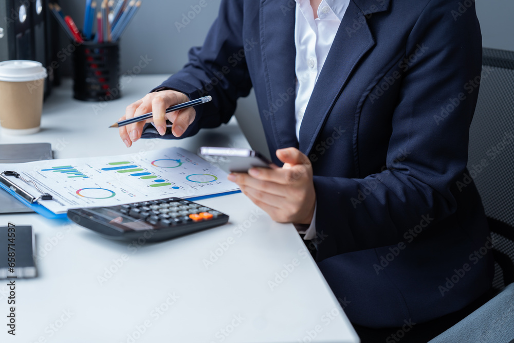 Business Documents concept: Employee Woman hands working with Smartphone, laptop, calculator, and chart on paper at the office. Business Documents concept: Employee Woman hands working with Smartphone, laptop, calculator, and chart on paper at the office.