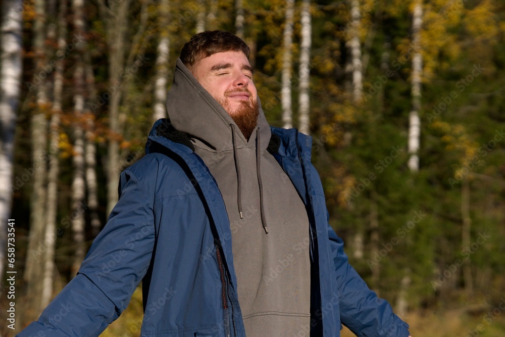 Portrait of young happy man in golden autumn forest at sunny fall day