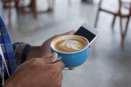 Close up of Asian man holding a cup of coffee and mobile phone. Technology and morning routine concept
