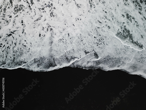White waves on a black sand beach in a volcanic island in Iceland from a drone view