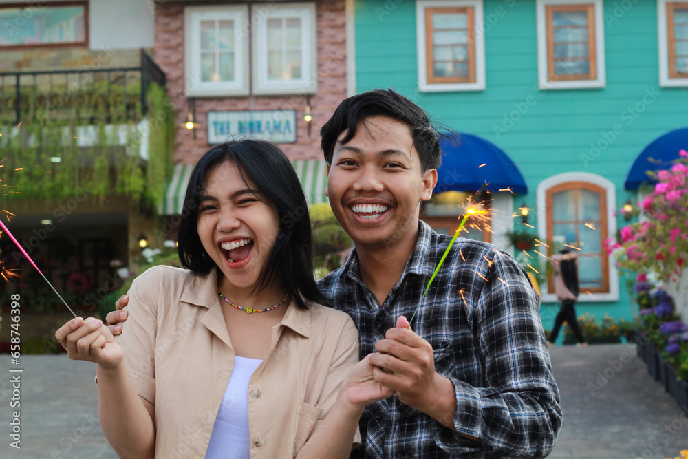 excited asian young couple having fun holding burning sparkler with smile and scream in the house yard wearing stylish clothes and flannel excited asian young couple having fun holding burning sparkler with smile and scream in the house yard wearing stylish clothes and flannel