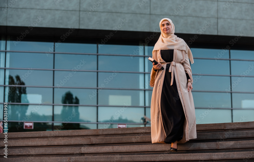 A successful Muslim business woman in hijab walking near the office building.