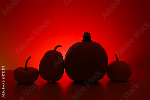 Four little pumpkins black silhouettes stands on surface in dark. Back wall is highlighted red with shadows. Holiday background with copy space for Halloween or Thanksgiving Day.