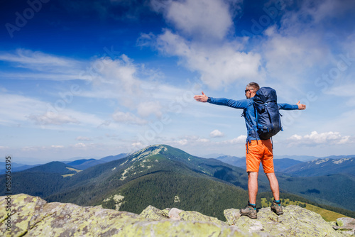 hiker at the top of the mountain with his hands raised enjoy sunny day