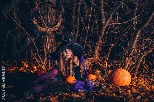 Halloween. Little witch with pumpkins in a dark forest.