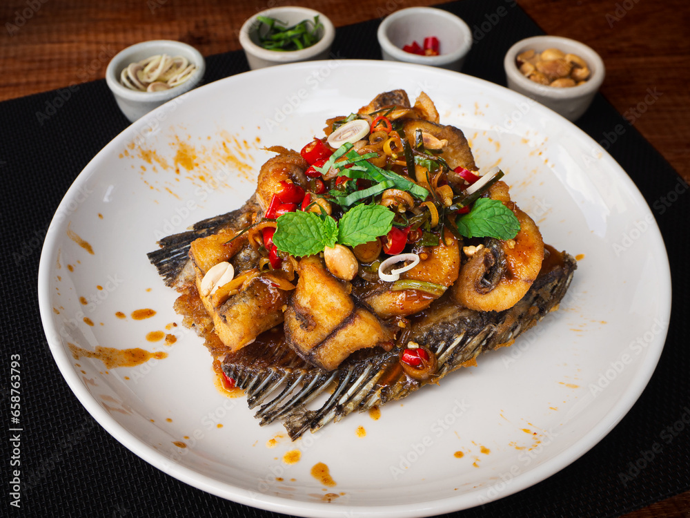 Deep fried fish with herb and spicy sauce in plate on wooden background. Thai Food