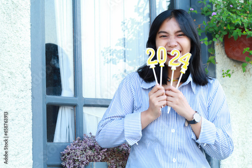 excited young woman celebrate new year eve with holding 2024 number candle  attractive female screaming to camera and standing over vintage house