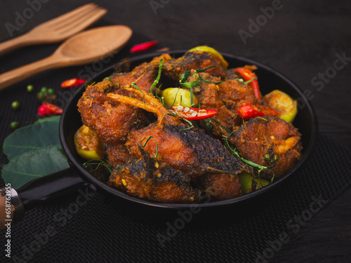 Stir fried catfish with herb and spicy sauce in pan on wooden background. Traditional Thai southern food