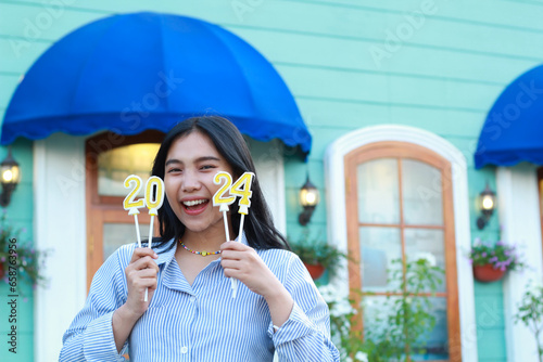 laughing asian young woman looking to camera enjoy 2024 new year eve celebration with holding 2024 number candle and standing in outdoor yard of vintage house