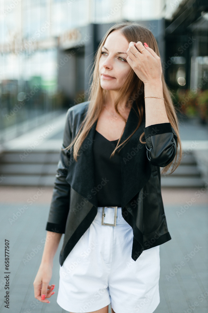A girl with long blond hair, wearing a black top, white shorts, poses against a background of a gray wall. Young woman walking through a park with modern architecture and landscape design A girl with long blond hair, wearing a black top, white shorts, poses against a background of a gray wall. Young woman walking through a park with modern architecture and landscape design