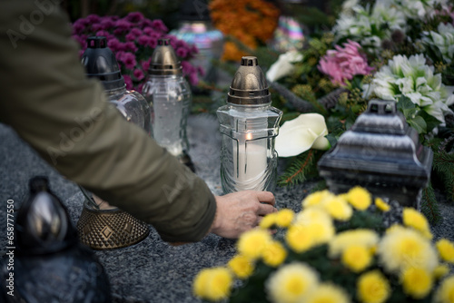 Hand placing a lit grave candle among flowers on a tombstone, close-up, Poland, November 1 — All Saints' Day (also known as All Souls' Day / Day of the Dead)