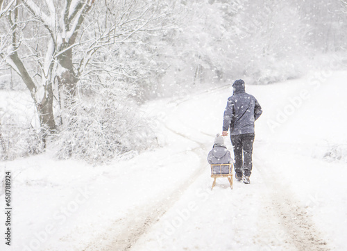 A father sledding his child on the snow winter day by snowfall. Family vacation in winter.