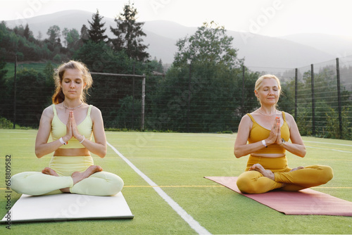 Two woman practicing yoga outdoors Mother and adult daughter exercising together. Mature female and young girl having healthy activities. Family meditation, strength training in mountains