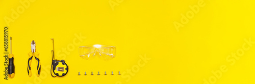 Set of tools, screwdriver, cutting pliers, tape measure, protective glasses and screws on yellow background, banner, flat lay. photo