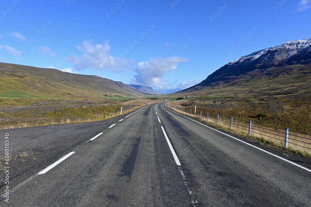 Ring Road near Akureyri, Iceland receding into distant curve between volcanoes under sunny morning autumn sky.