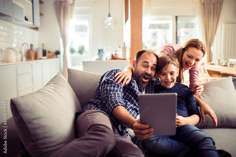 Young Caucasian family using a tablet and having fun on the couch at home Young Caucasian family using a tablet and having fun on the couch at home