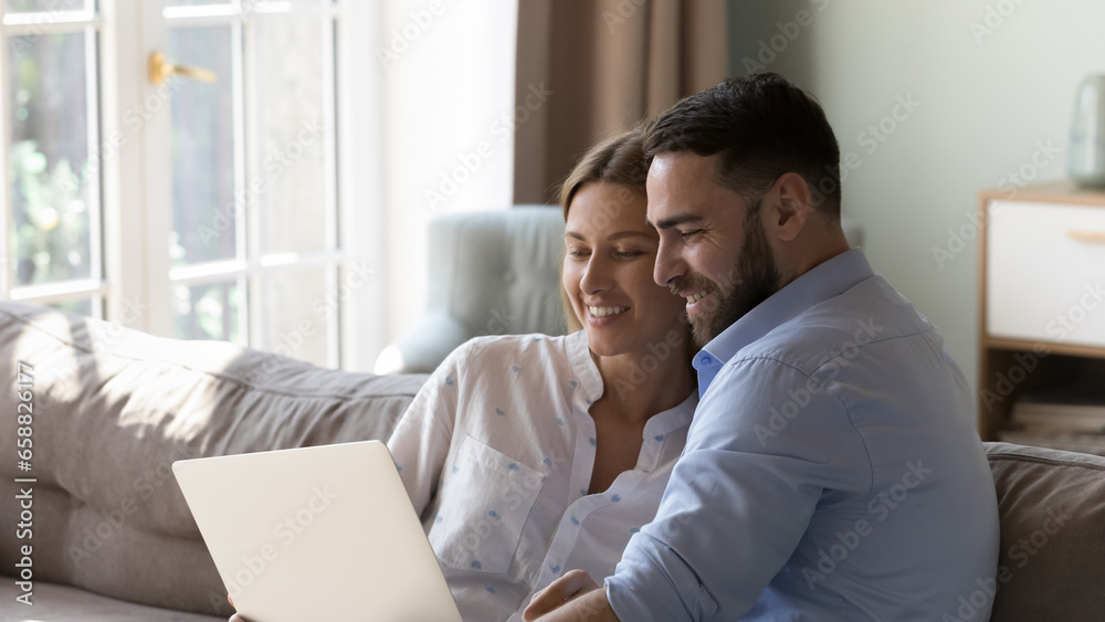 Happy married couple resting on sofa with gadget, using Internet app on laptop together, watching movie, interactive TV channel, online broadcasting, making order, enjoying communication. Banner shot Happy married couple resting on sofa with gadget, using Internet app on laptop together, watching movie, interactive TV channel, online broadcasting, making order, enjoying communication. Banner shot