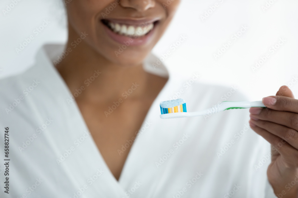 Crop close up of smiling african American girl put toothpaste on toothbrush clean brush teeth in home bathroom, happy biracial young woman take care of oral hygiene, do daily morning routine in bath Crop close up of smiling african American girl put toothpaste on toothbrush clean brush teeth in home bathroom, happy biracial young woman take care of oral hygiene, do daily morning routine in bath