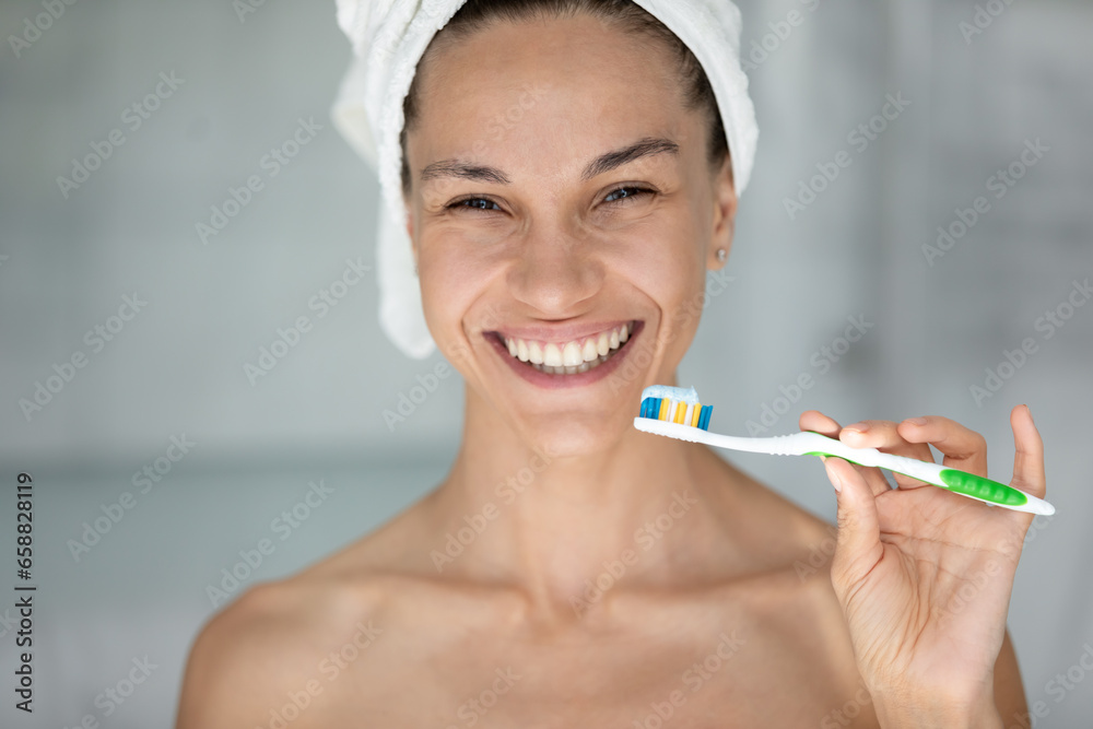 Portrait of smiling young woman in head towel brush teeth with toothbrush and toothpaste in bathroom, happy female after shower take care of oral hygiene, do daily morning routine in home bath Portrait of smiling young woman in head towel brush teeth with toothbrush and toothpaste in bathroom, happy female after shower take care of oral hygiene, do daily morning routine in home bath