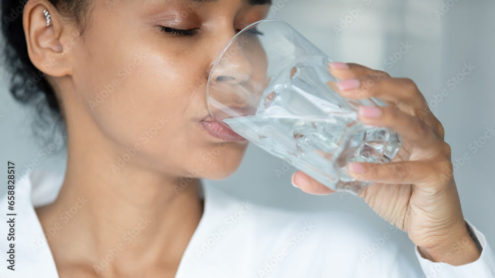 Close up of african American young woman feel thirsty drink clear pure mineral water from glass, biracial girl enjoy clean still aqua for body refreshment, hydration, healthy lifestyle concept Close up of african American young woman feel thirsty drink clear pure mineral water from glass, biracial girl enjoy clean still aqua for body refreshment, hydration, healthy lifestyle concept