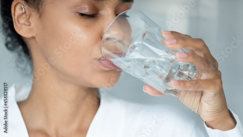 Close up of african American young woman feel thirsty drink clear pure mineral water from glass, biracial girl enjoy clean still aqua for body refreshment, hydration, healthy lifestyle concept