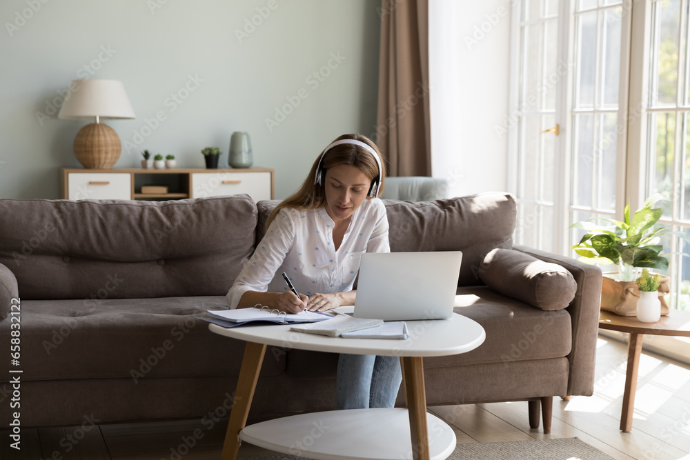 Focused millennial laptop user woman in wireless earphones writing notes at computer, watching learning webinar, workshop, blog, studying from home. Freelance employee talking to client on video call Focused millennial laptop user woman in wireless earphones writing notes at computer, watching learning webinar, workshop, blog, studying from home. Freelance employee talking to client on video call