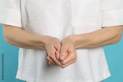 Woman cracking her knuckles on turquoise background, closeup. Bad habit