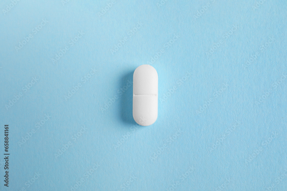 One white pill on light blue background, top view One white pill on light blue background, top view