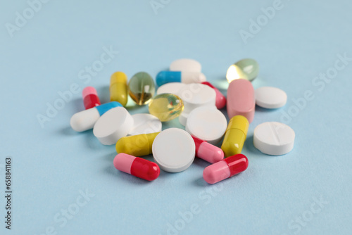 Pile of colorful pills on light blue background, closeup