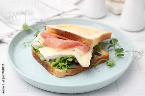 Tasty sandwich with brie cheese and prosciutto on white tiled table, closeup