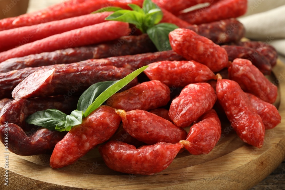 Different thin dry smoked sausages and basil on wooden board, closeup Different thin dry smoked sausages and basil on wooden board, closeup