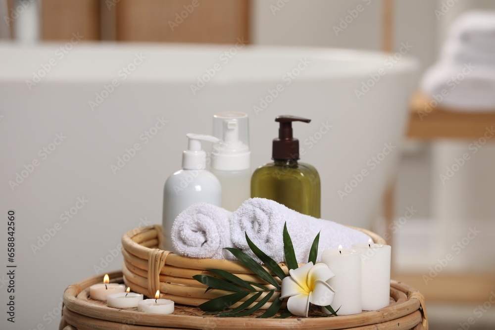 Spa products, burning candles, plumeria flower and tropical leaf on table in bathroom