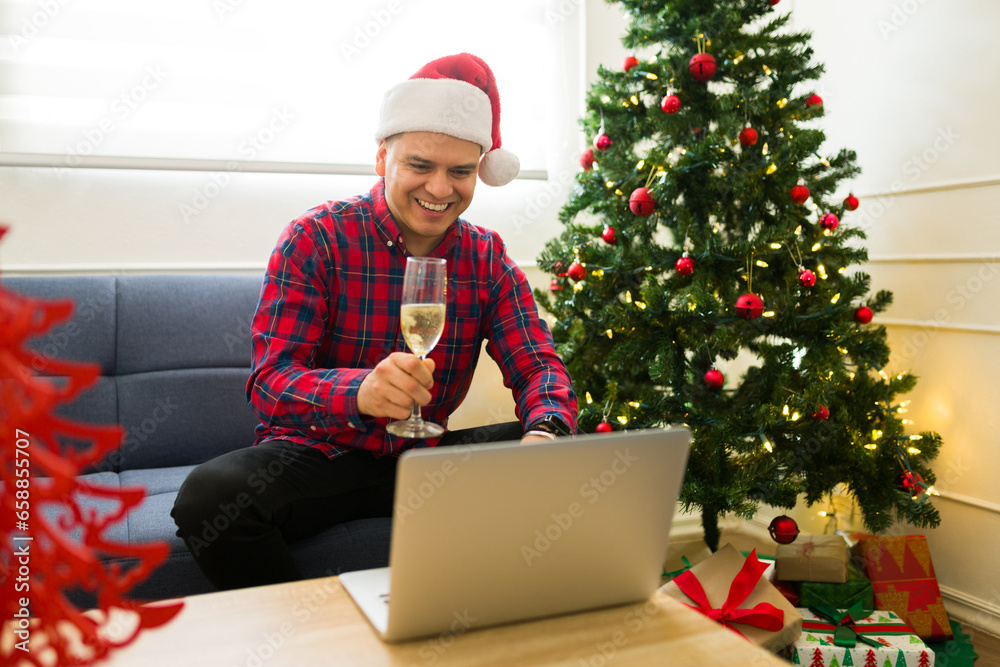 Latin man saying cheers with champagne celebrating christmas on a video call Latin man saying cheers with champagne celebrating christmas on a video call