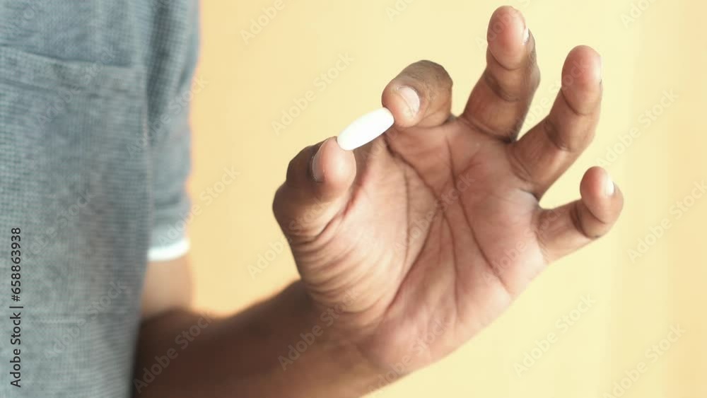 Close up of man hand holding capsule against orange background Close up of man hand holding capsule against orange background