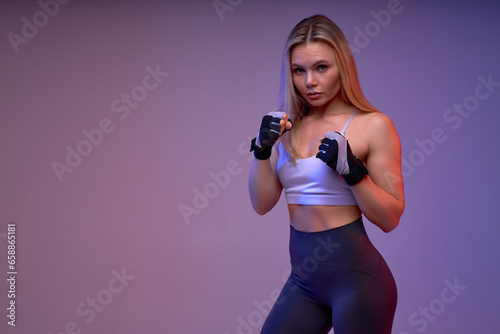beautiful serious confident blonde female boxer looking at the camera, preparing to kick, close up portrait, isolated violet background, self-defense, strength training, motivation, copy space © alfa27