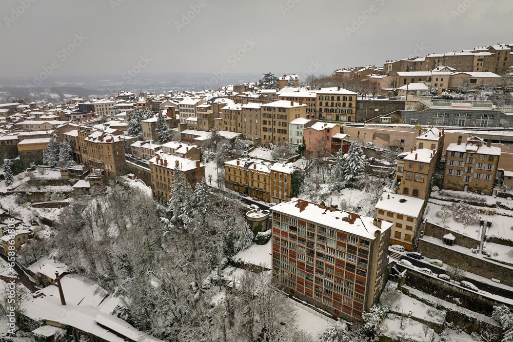 Aerial winter landscape of dense historic center of Thiers town in Puy-de-Dome department, Auvergne-Rhone-Alpes region in France. Rooftops of old buildings and narrow streets at snowfall