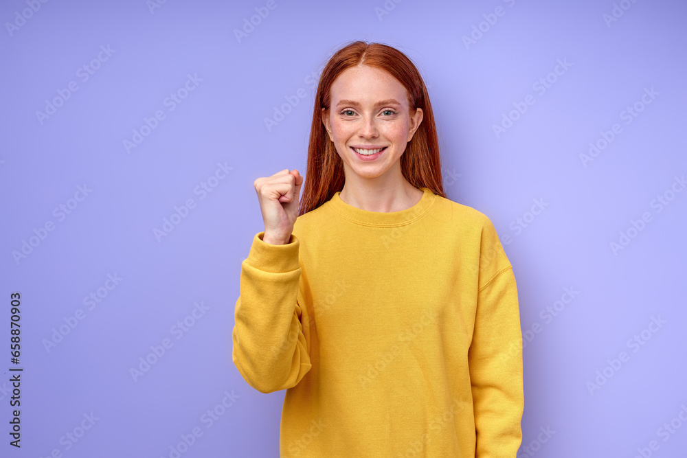 Young deaf mute woman using sign language on blue background, showing letter A, smiling girl with clenched fist looking at camera body language closeup portrait