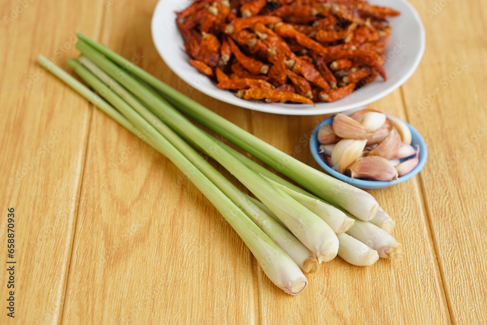 Fresh lemongrass, bowls of garlice  and dried chillies on brown wooden floor. Concept, food ingredients, prepared for cooking. Herbal plants in Thai kitchen for various menus.              